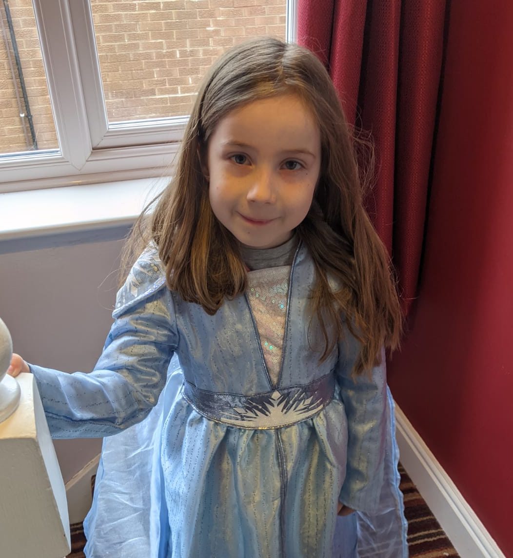 Abigail's best friend Alys stands at the top of the stairs with her right hand on the bannister. Alys is wearing a pale blue and white princess dress and is smiling up at the camera.