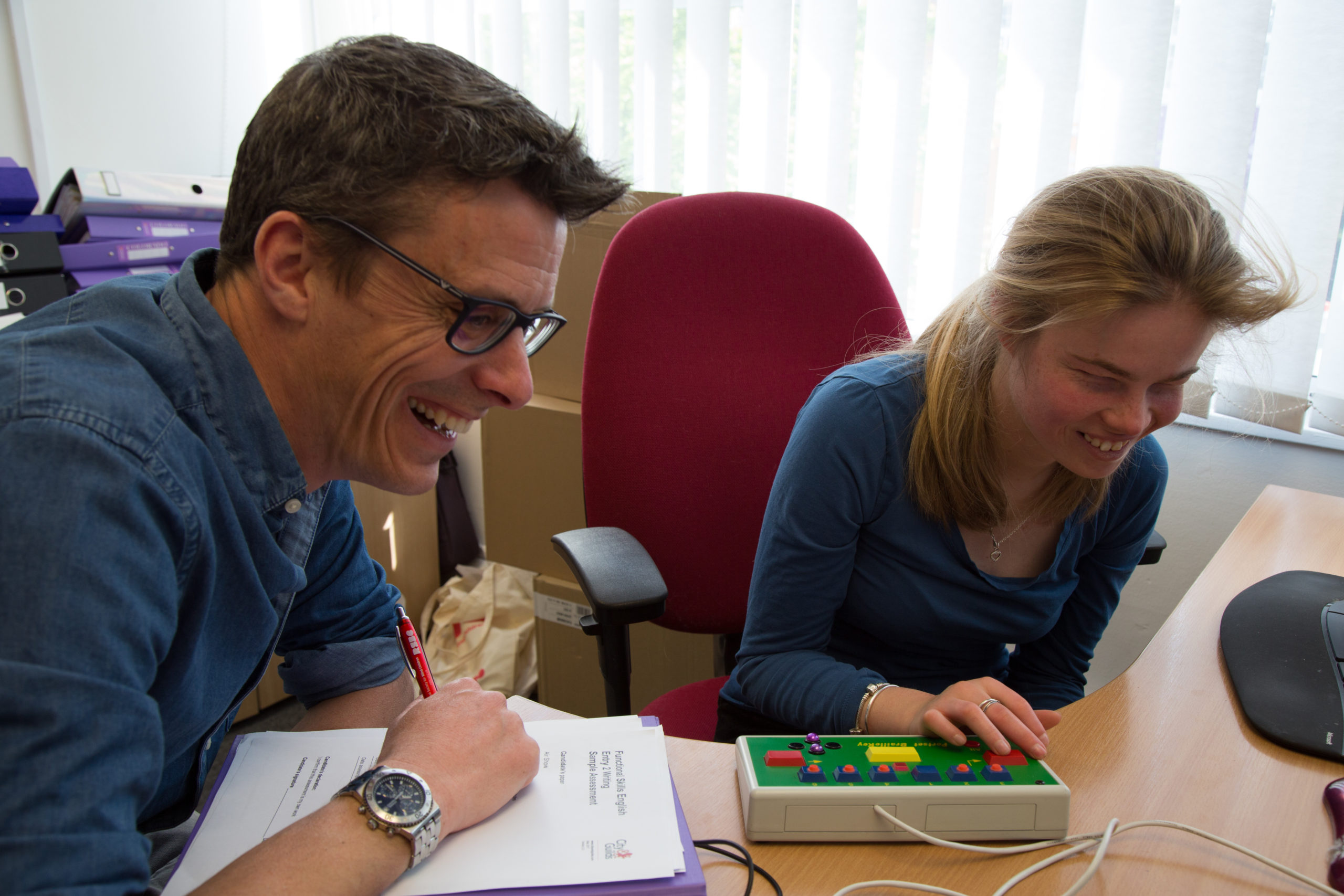 A Dorton College staff member sits at a desk next to a female student, both smiling as they carry out an activity