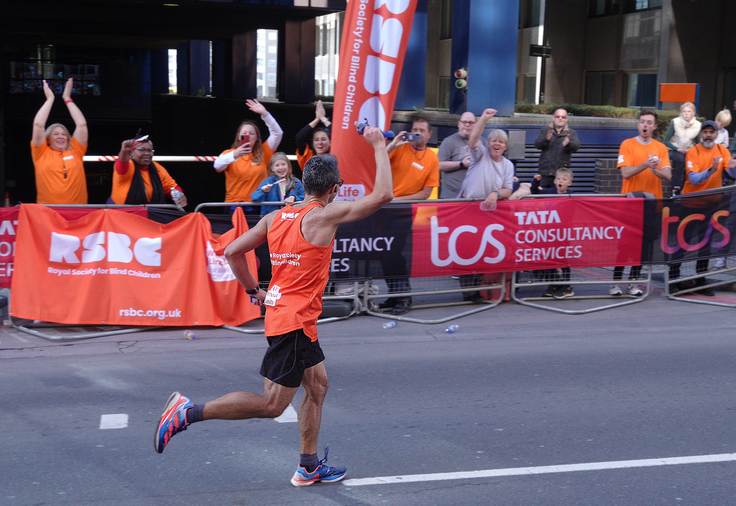 A RSBC runner waving at people standing up at the RSBC cheer point