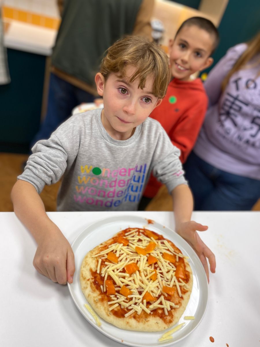 An excited child in front of a plate with a pizza ready to go in the oven