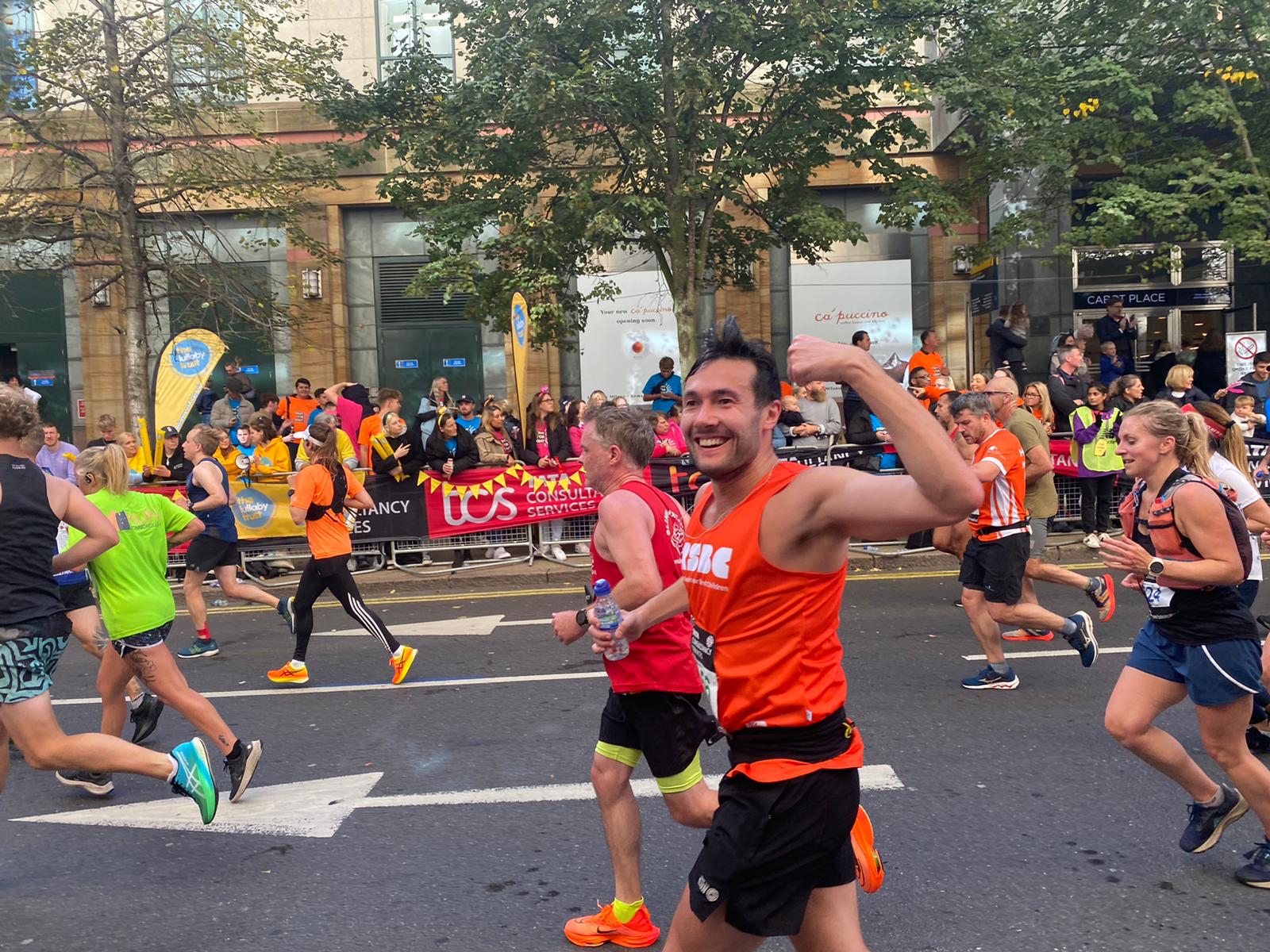 A man with a RSBC T-shirt running with his arm up looking happy