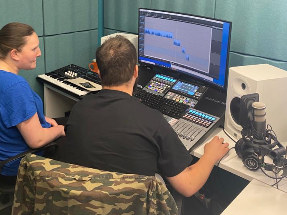 Two people in a recording studio looking at a monitor with a microphone next to them