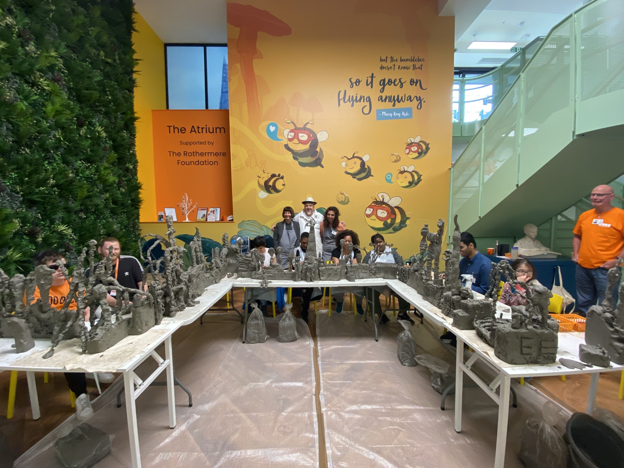 a group of people seating behind tables with sculptures with a colourful wall in the background