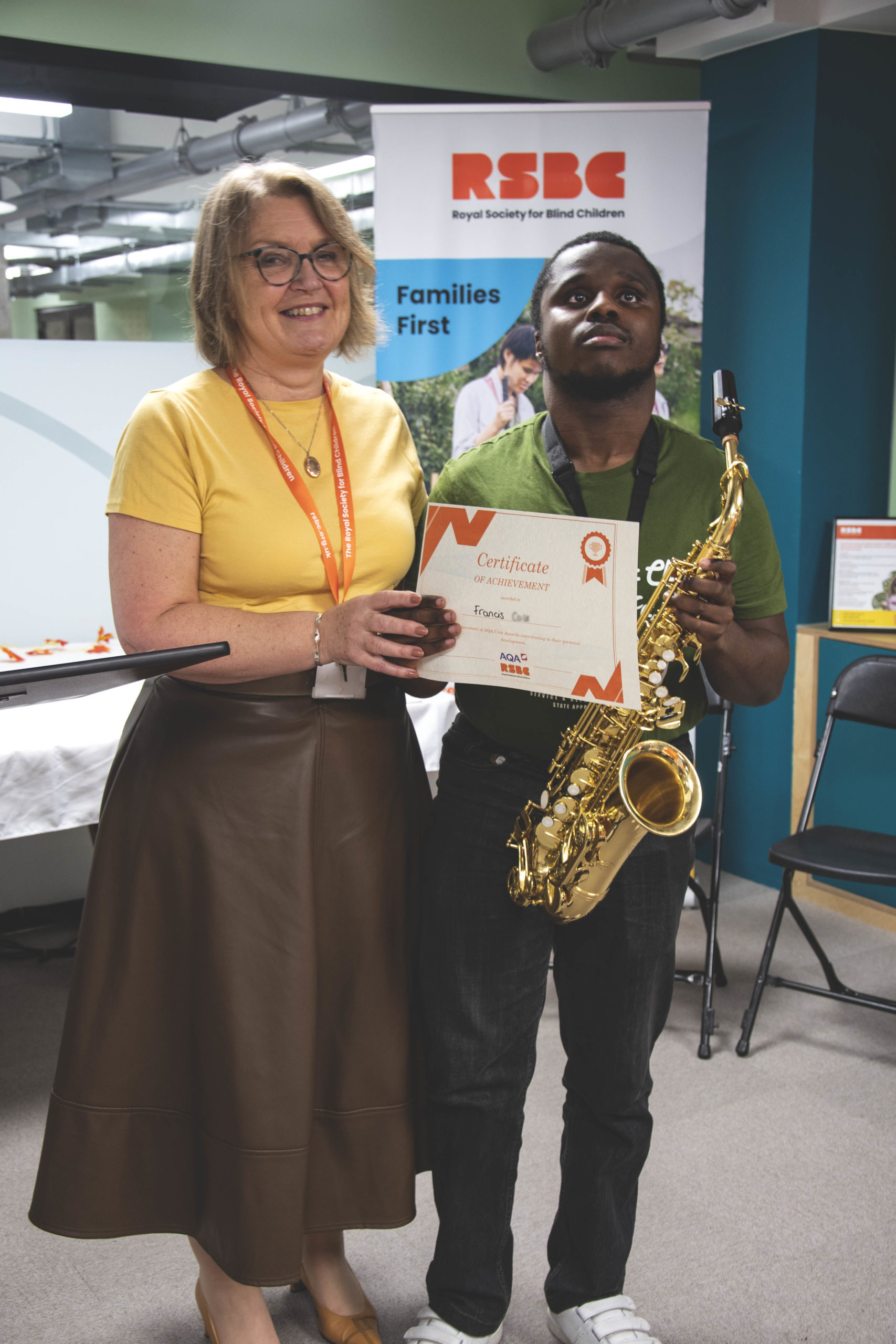 A young man with a saxophone receiving a certificate standing up next a woman