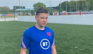 A young man wearing a football outfit standing up in a a football ground