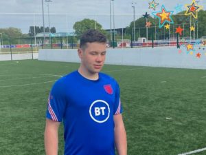 A young man wearing a football outfit standing up in a a football ground