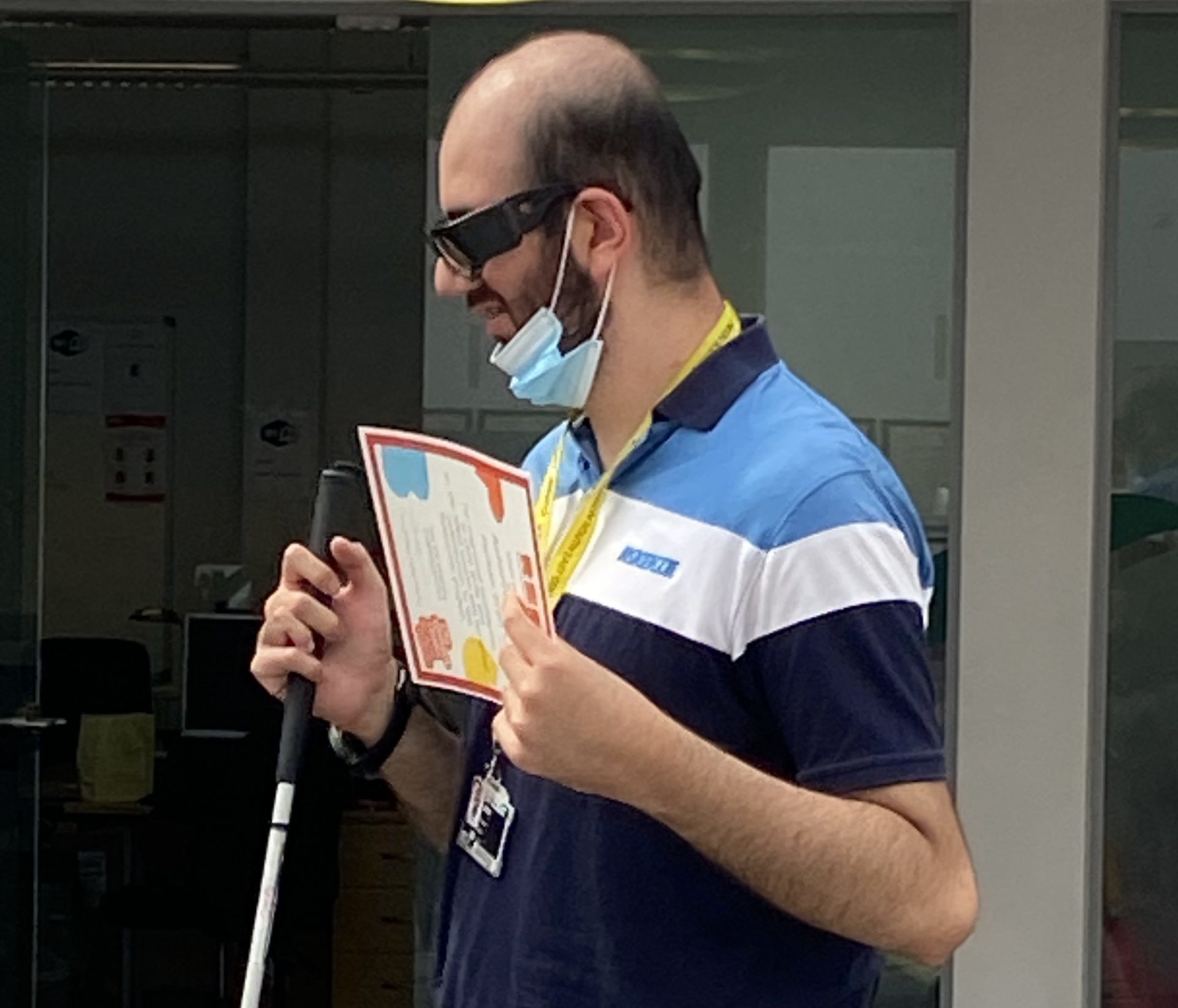 A man standing up with a white cane holding a certificate