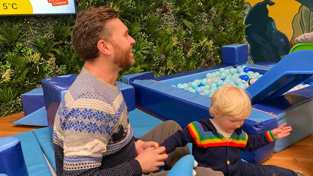 A dad smiling next his son next to a ball pit