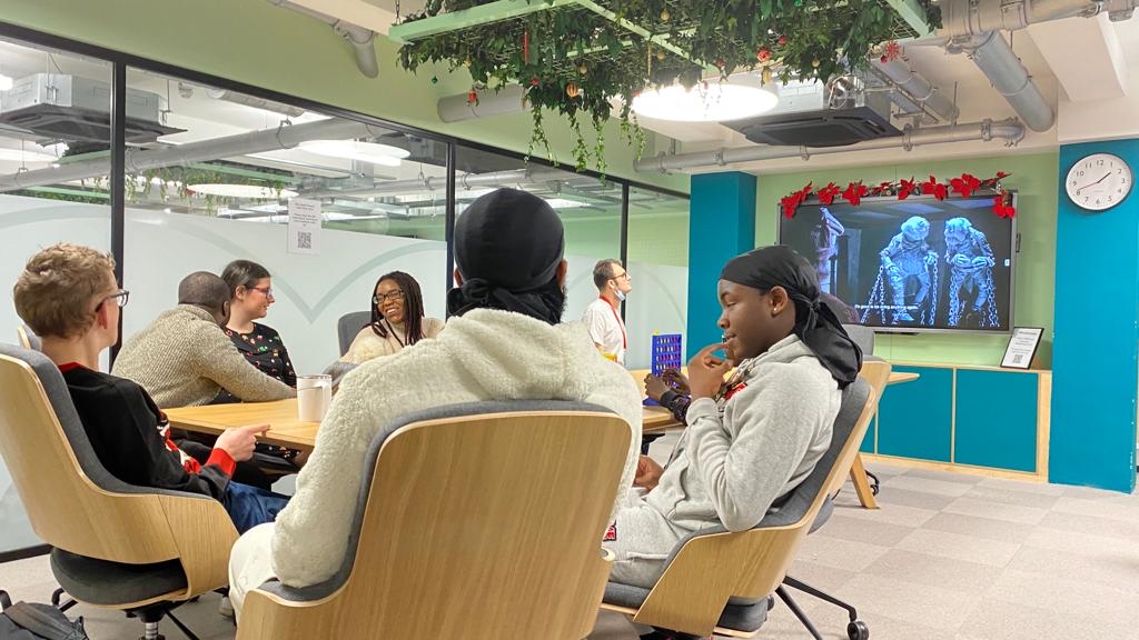 A group of young people gathered around a table with the TV on