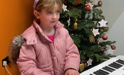 A girl playing piano next to a Christmas tree