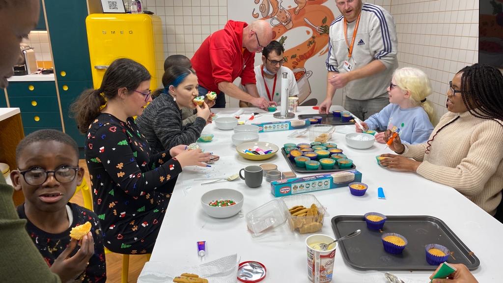 A group of people sitting around a table decorating cupcakes and gingerbread