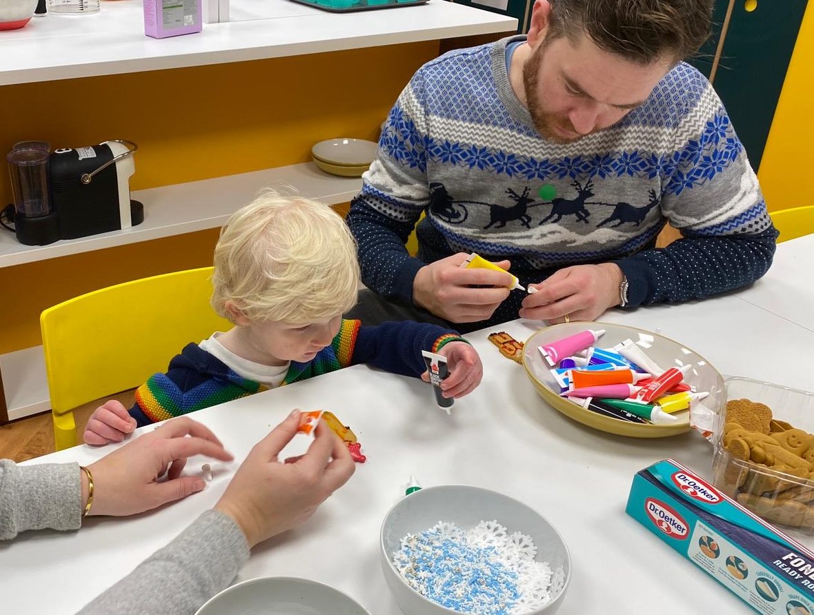 A dad with his child decorating gingerbread man at a table