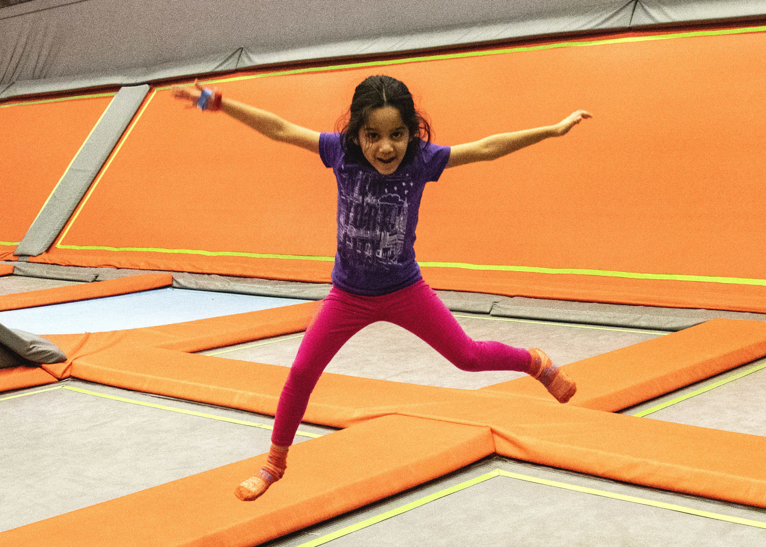 A young girl looking happy jumping on a trampoline