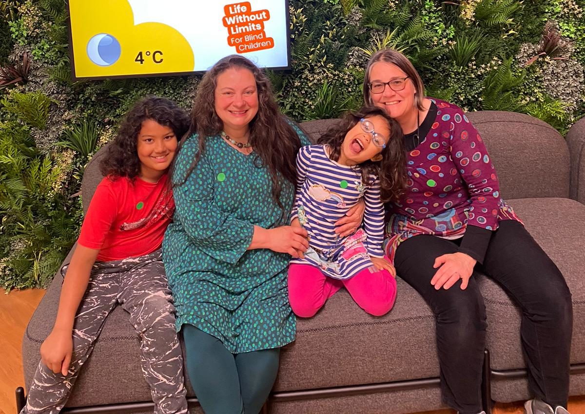 A family including 2 young girls seating on a sofa and smiling at camera