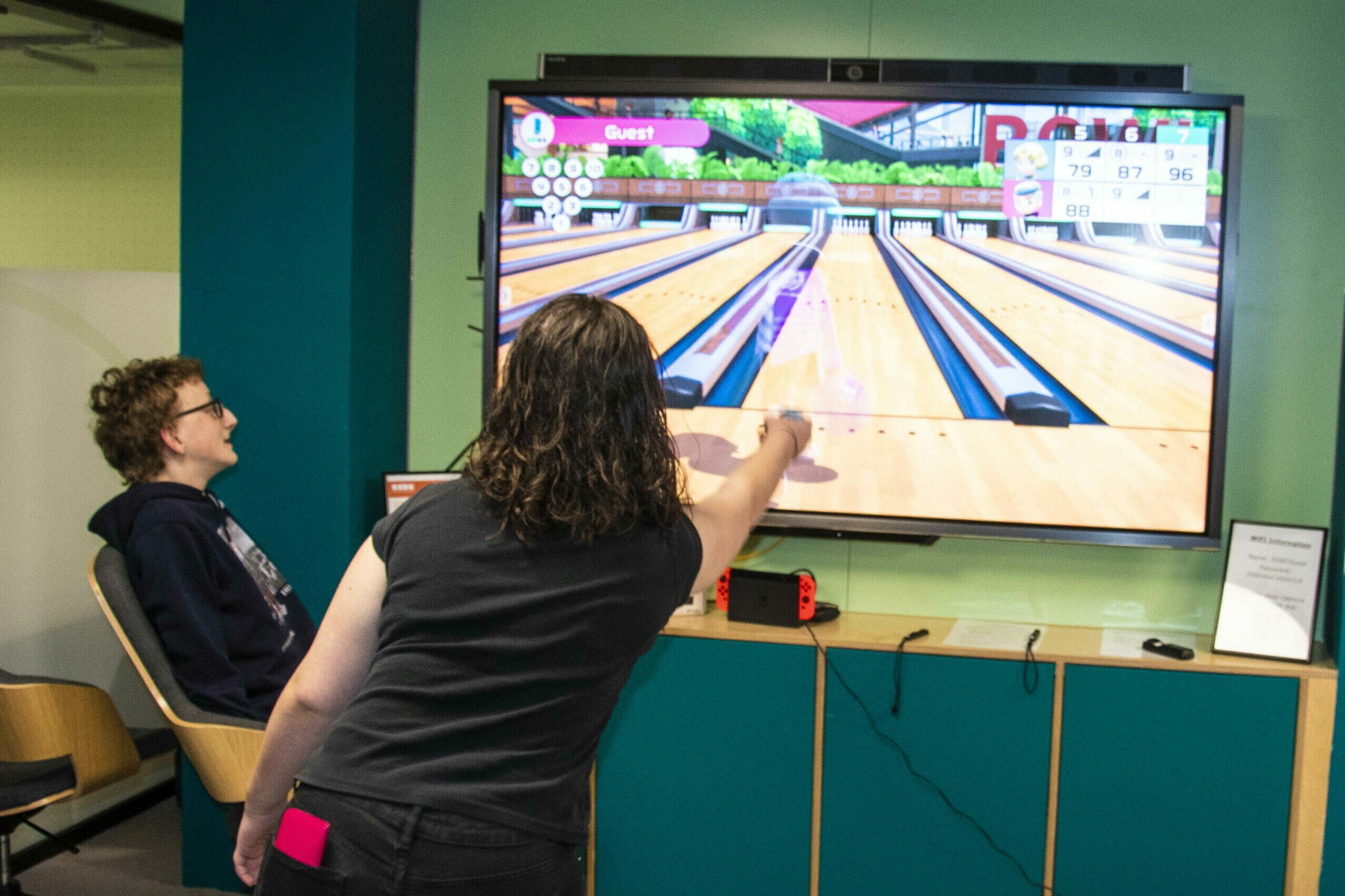 2 young persons in front of a large screen doing video games