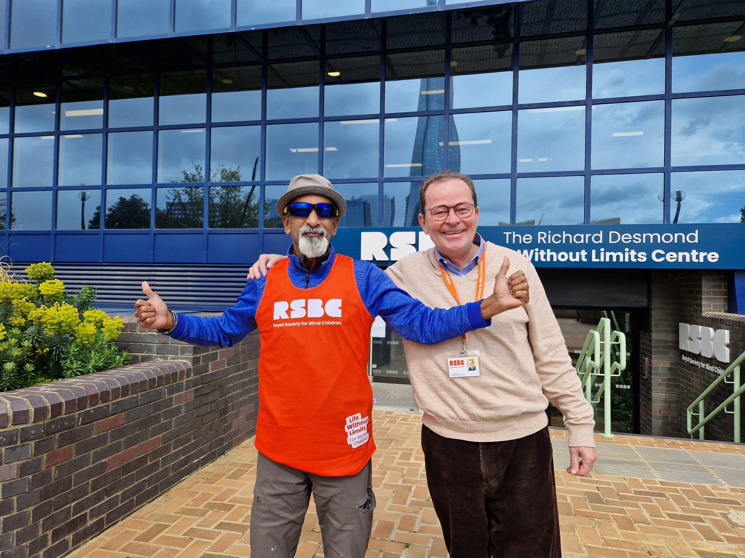 2 men sanding in front of the RSBC Life Without Limits Centre . The person on the left is wearing an RSBC T-shirt