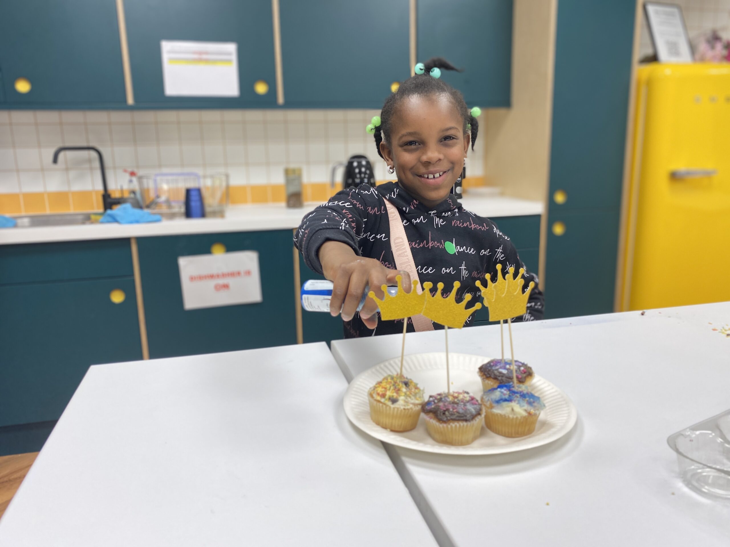 A child smiling and showing fairy cakes with royal decoration