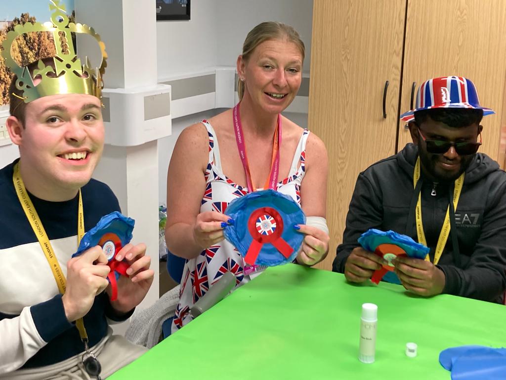 2 young people with a woman in the middle smiling with royal-themed accessories