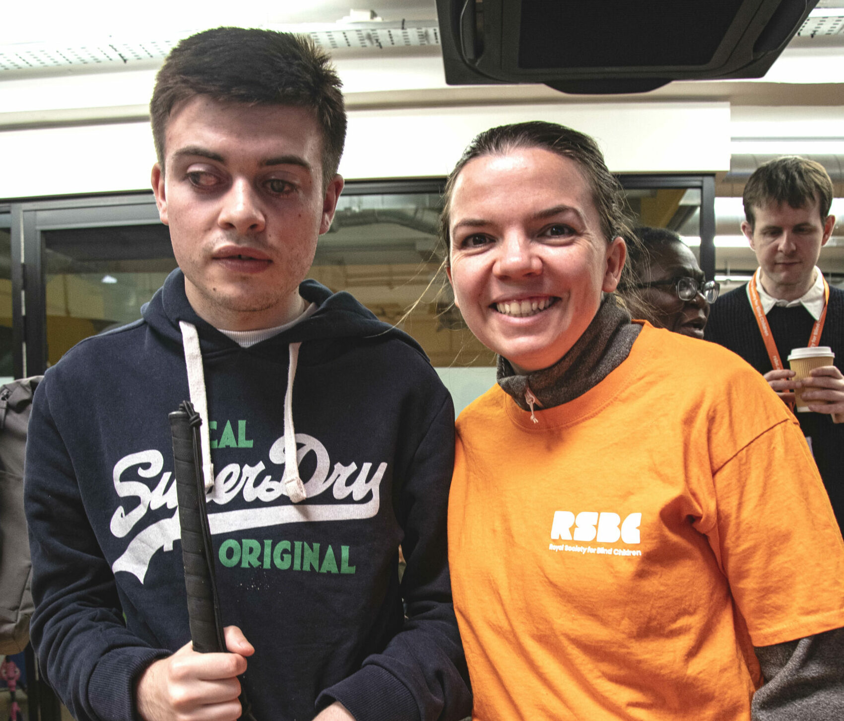 A young person with a cane standing next to an RSBC volunteer