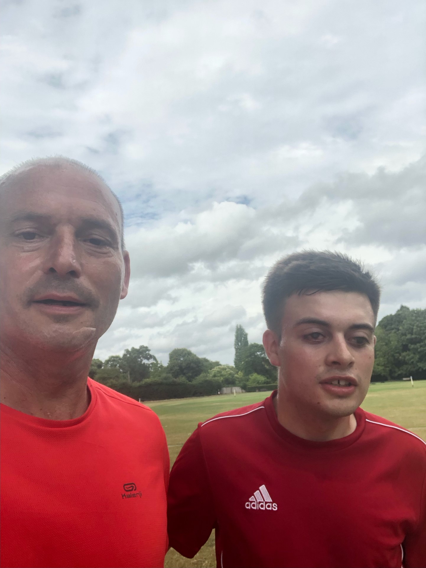 A young man and his dad in red running tops, running in the park