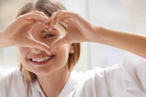 A young woman smiling and making a love heart sign with her hands.