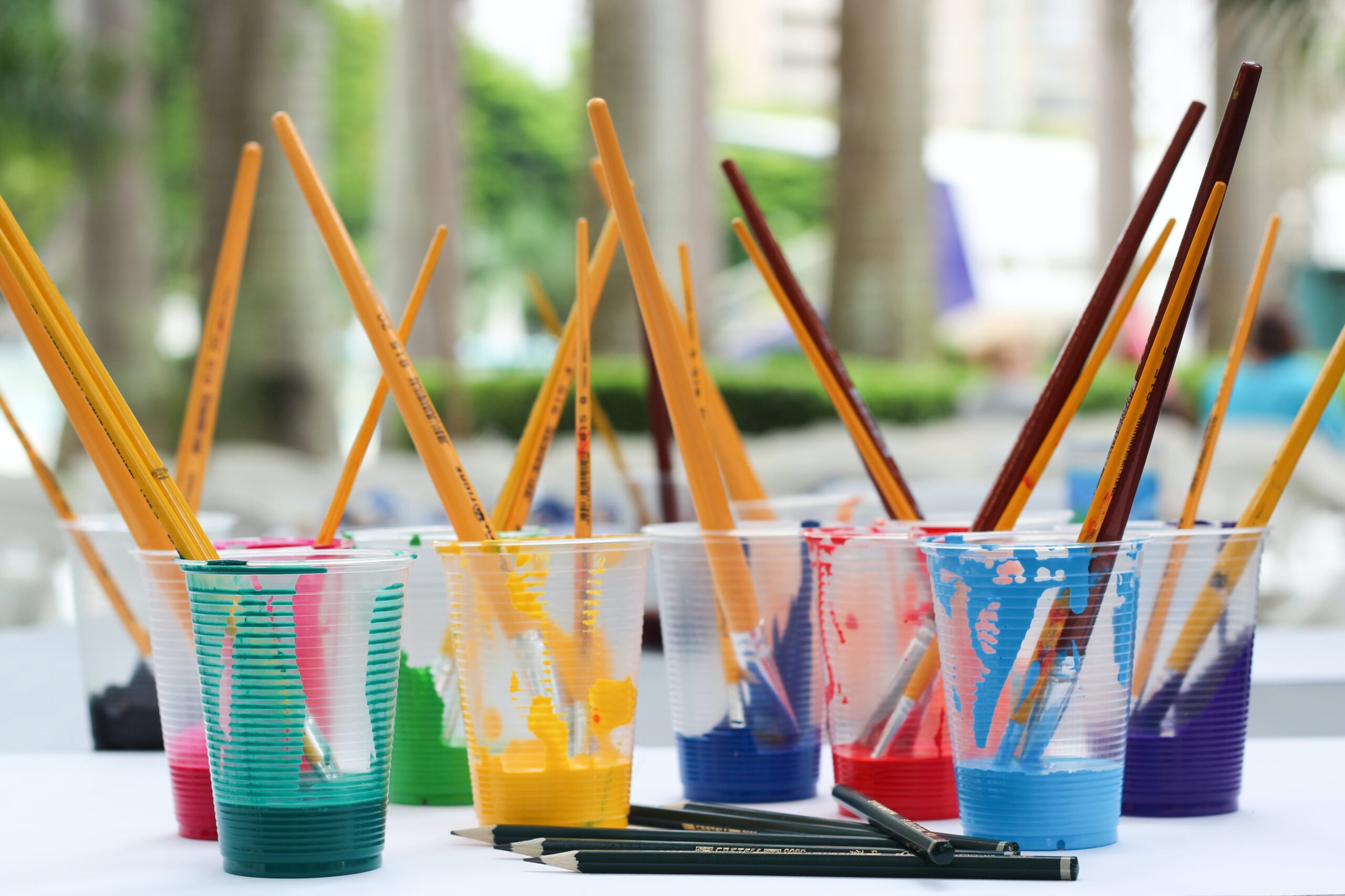 A group of different coloured glasses of paint with paint brushes