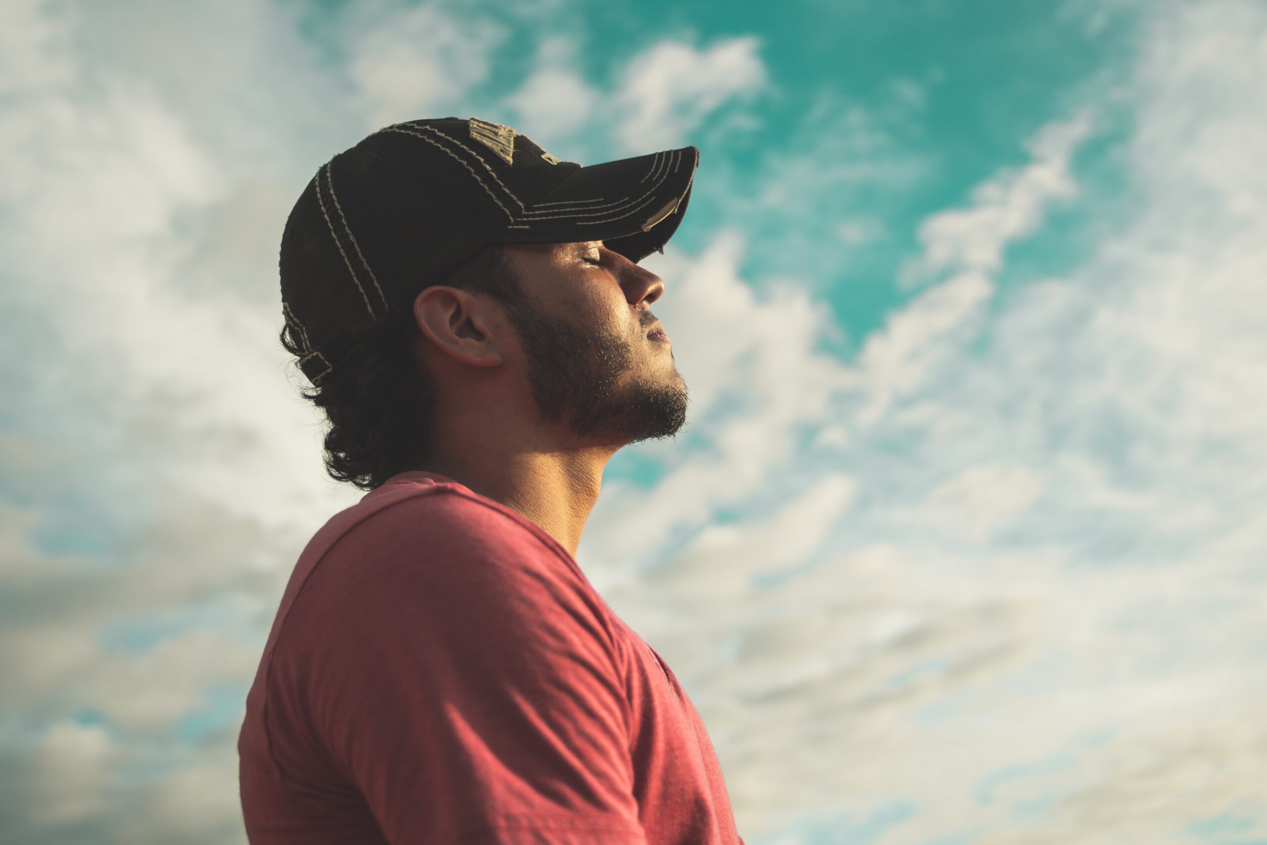 A young man, wearing a baseball cap, with his eyes closed and head pointing to the sky