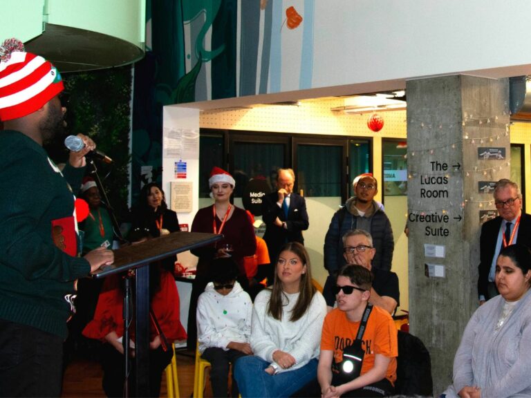 A young man wearing a christmas hat singing in front of an audience.