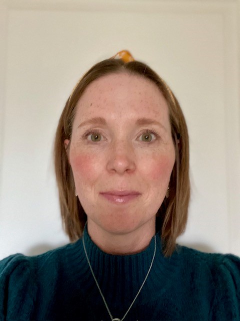 A headshot of a woman, Jessica, who has bobbed, straight, shoulder length brown hair and a serious expression as she looks straight ahead. She wears a blue turtle neck top and a silver necklace.