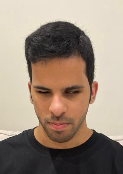 A head and shoulders image of Mohammed, a medium skinned young person with dark hair and stubble, wears a black T shirt as he looks downwards with a serious expression.