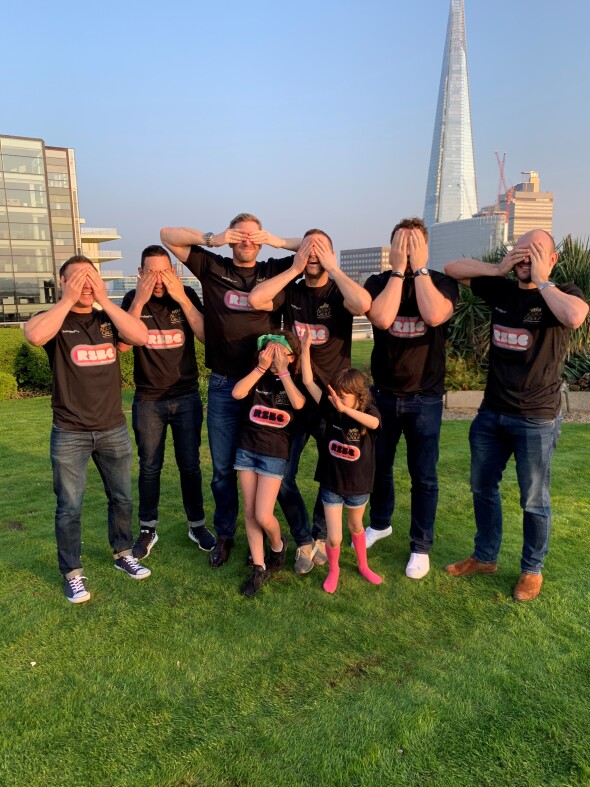 A group of people standing outside, posing with their hands over their eyes. The people are wearing RSBC T-shirts.