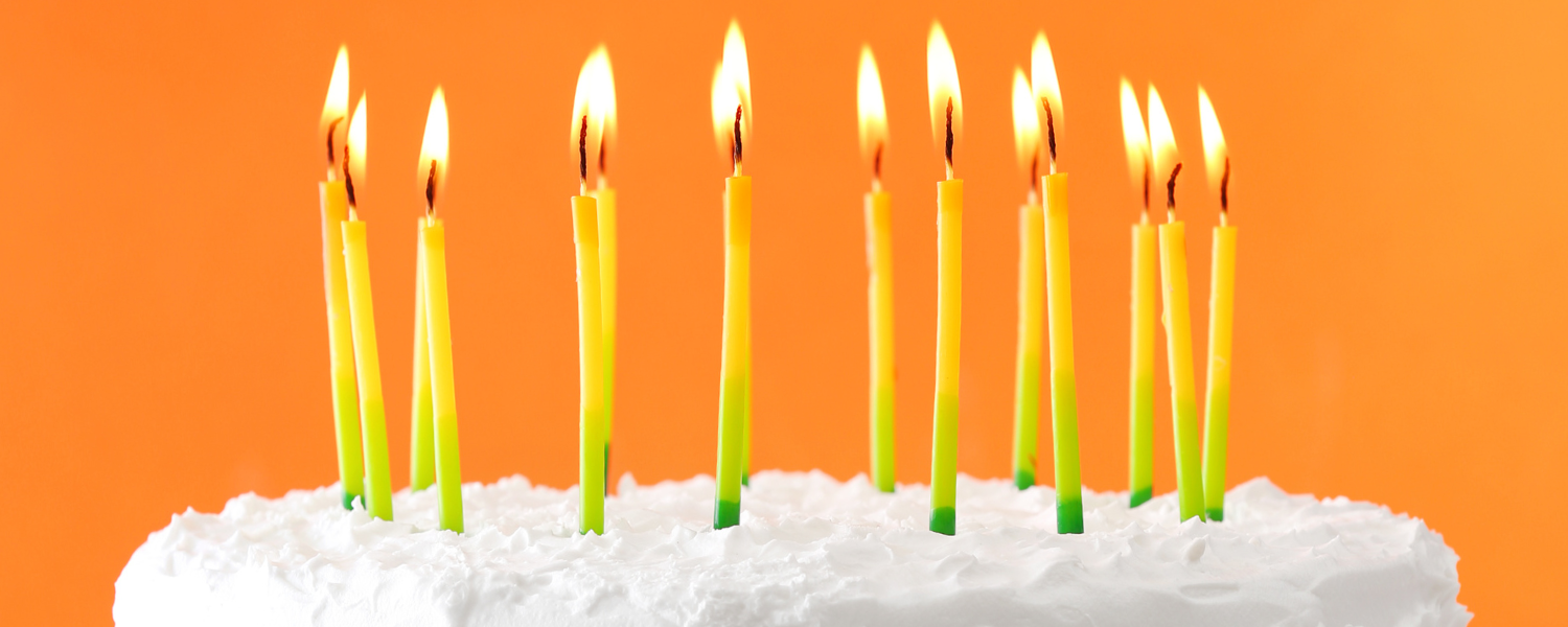 A Birthday cake with white icing and lit candles, against an orange background.