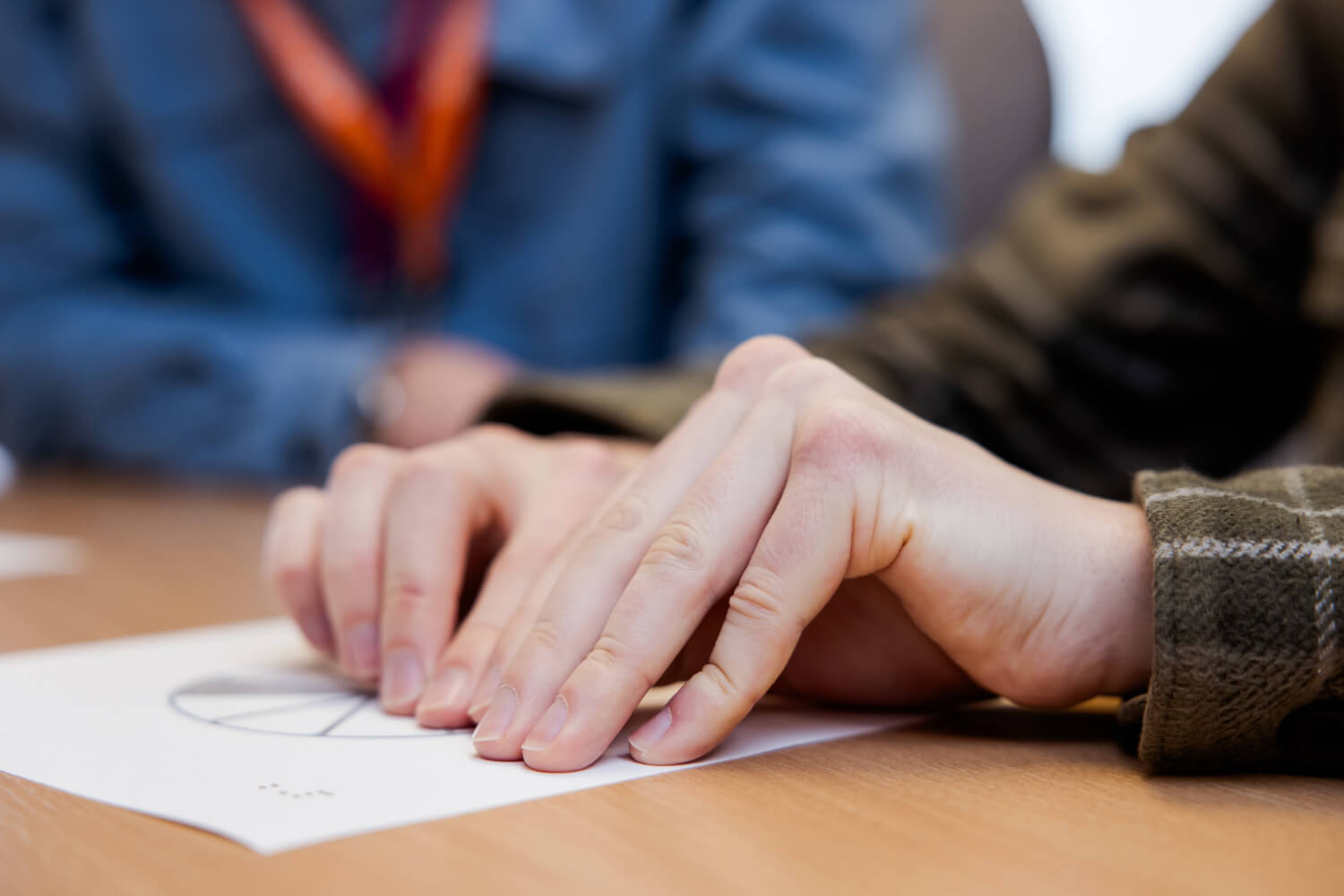 A student reads braille while an RSBC staff member with orange lanyards sits beside them