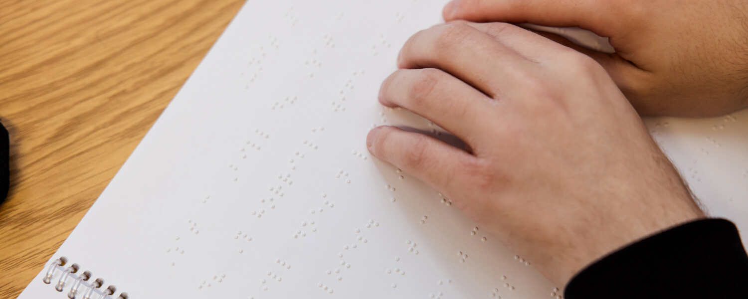 A student's hands reading a white braille book