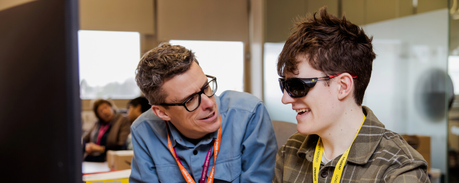 A light skinned male Dorton College student with brown hair wears dark glasses as a light skinned male RSBC staff member with grey hair and glasses talks to him. Both are smiling broadly.