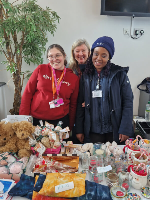 Two students and an RSBC staff member smile behind a table full of items to sell