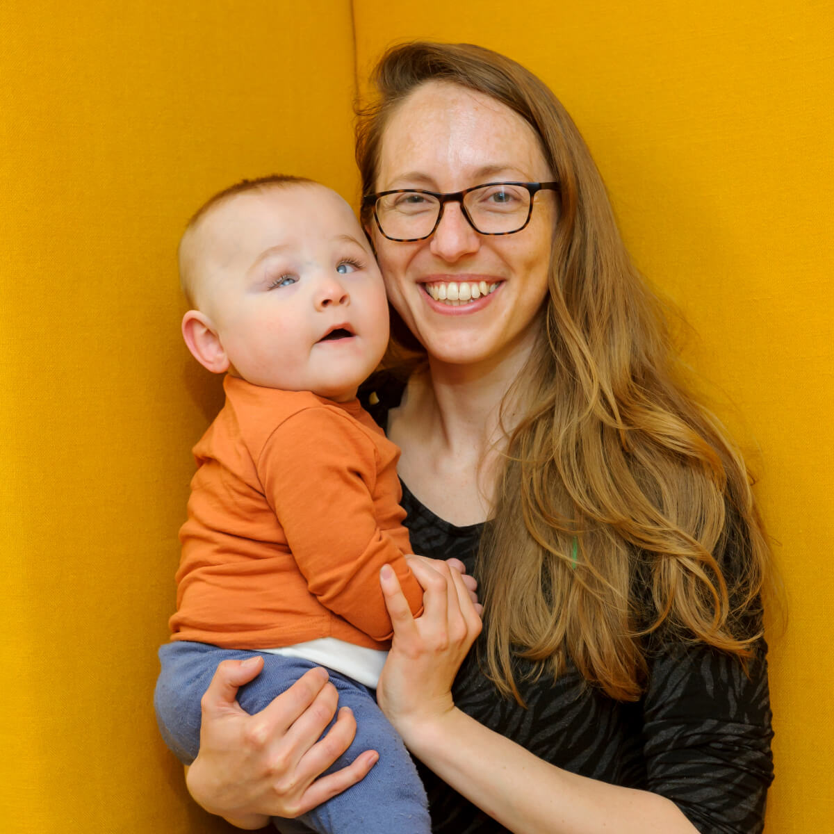 Mum with long hair holds young child in a bright orange T shirt