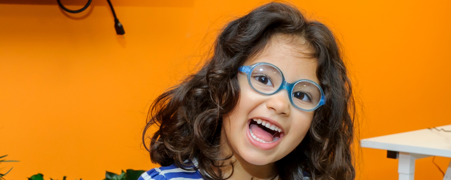 Young dark haired girl in blue glasses smiles as she plays the xyolophone.