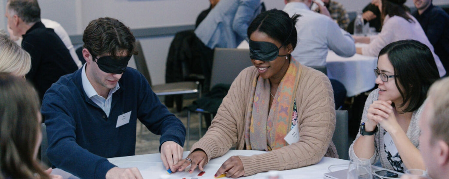 Two blindfolded work colleagues sit together and build Lego.