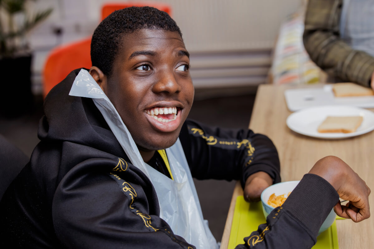 A male student with black hair eats cereal and smiles up at the camera