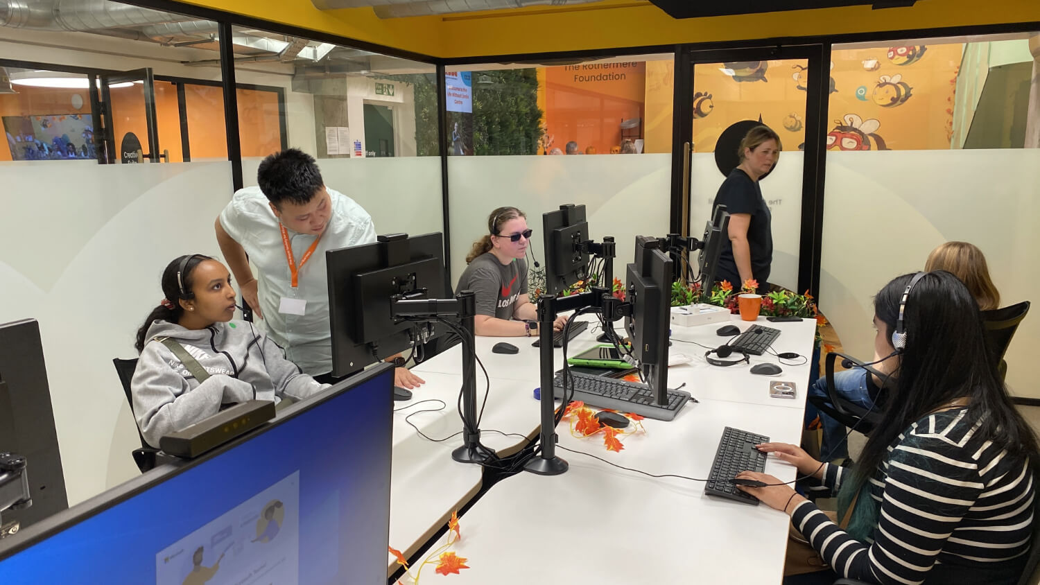 Six people sitting and standing near computer monitors spread around a table.