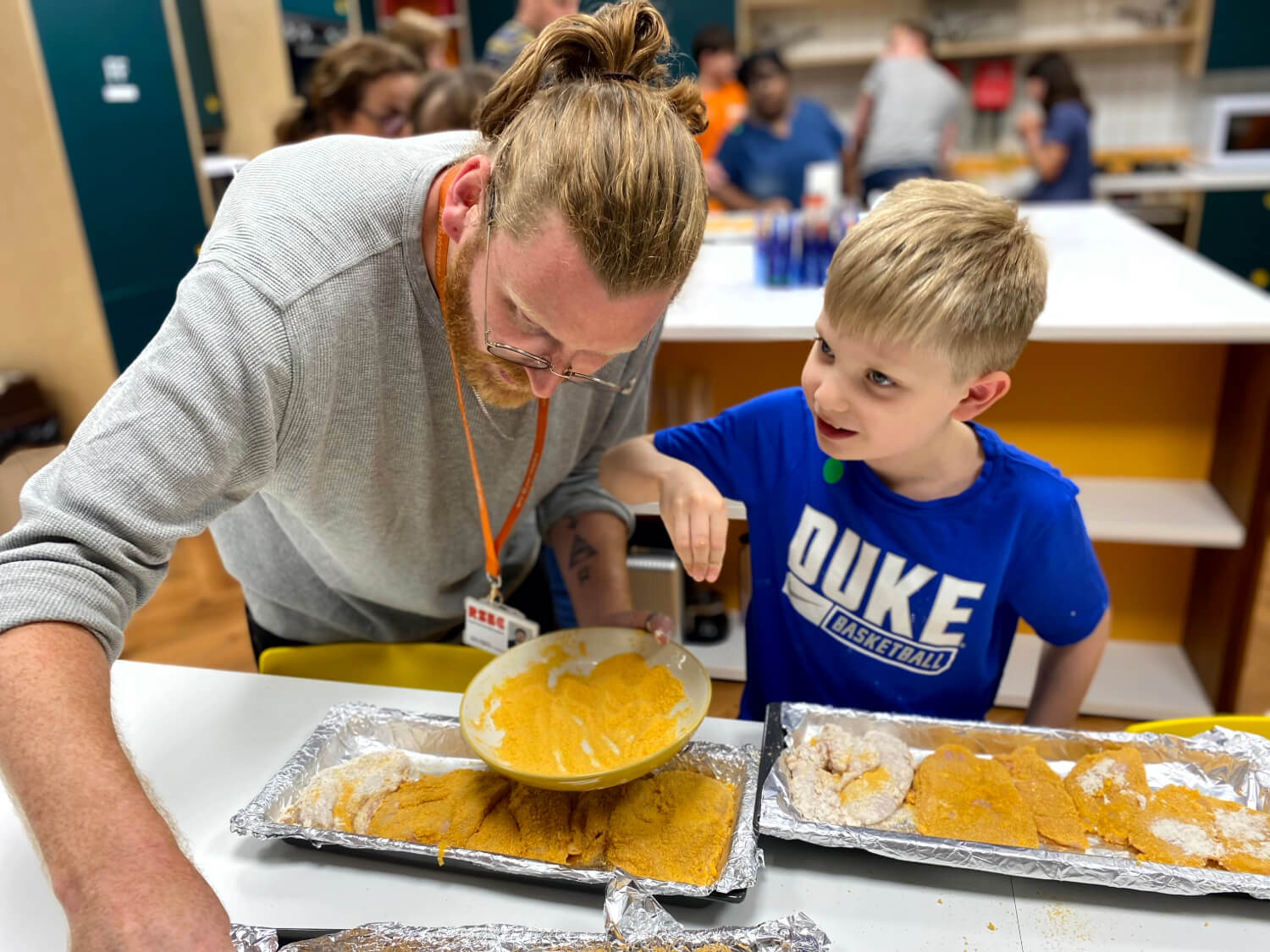 An RSBC staff member and a blond boy make food on silver trays