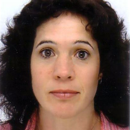 Alison, a light skinned woman with black curly hair and brown eyes, stares straight ahead into the camera with a serious expression. The background is white and she wears a patterned pink top.