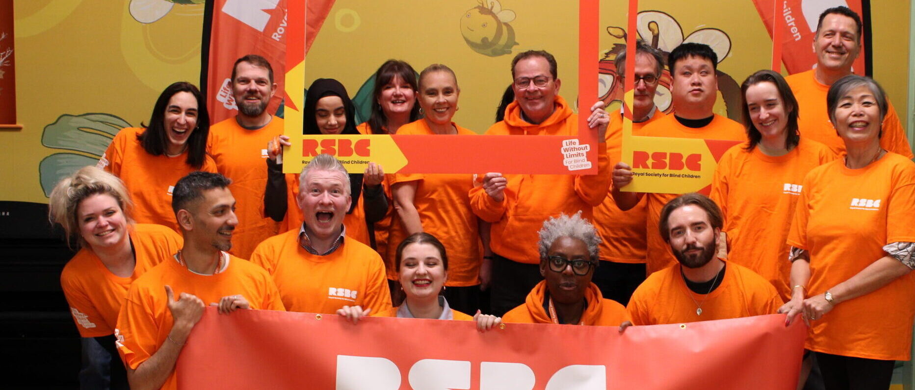 A group photo of RSBC staff members wearing orange RSBC branded t-shirts and holding RSBC banners.