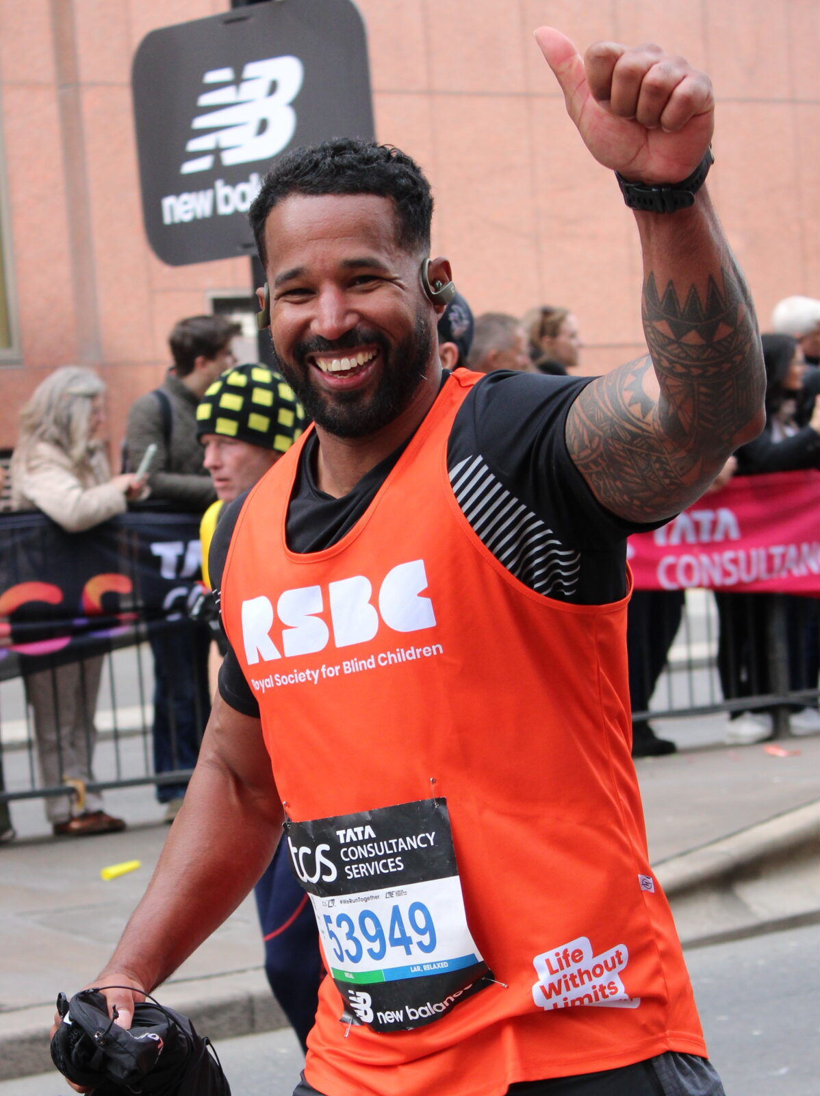 A man running the London Marathon wearing an orange RSBC vest. He is smiling at the camera with a thumbs-up hand gesture.