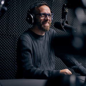 A man in a studio wearing headphones and speaking into a professional microphone.