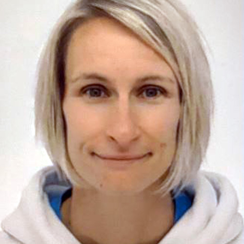 Tereza, a light skin toned person with a shoulder length light blonde bob hairstyle, stared straight ahead with a slight smile on her lips. She wears a white hoodie and is in front of a white background.