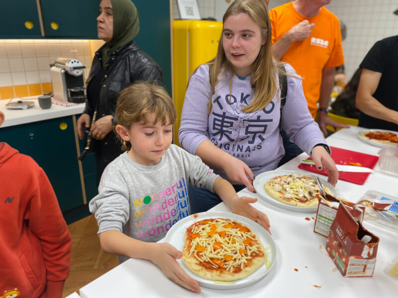 A young girl looks at a pizza she's made while a woman looks on.