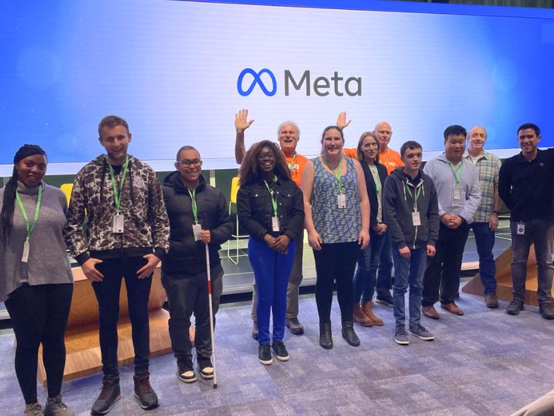 A group of RSBC representatives and beneficiaries on stage in front of a screen that reads 'Meta'.