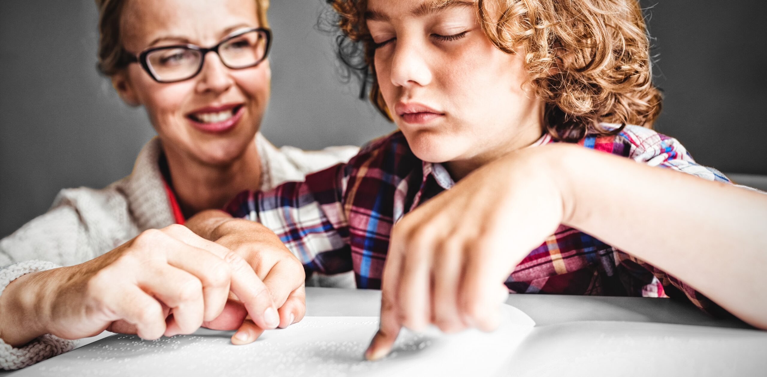 A young boy reading braille with the assistance of a teacher.